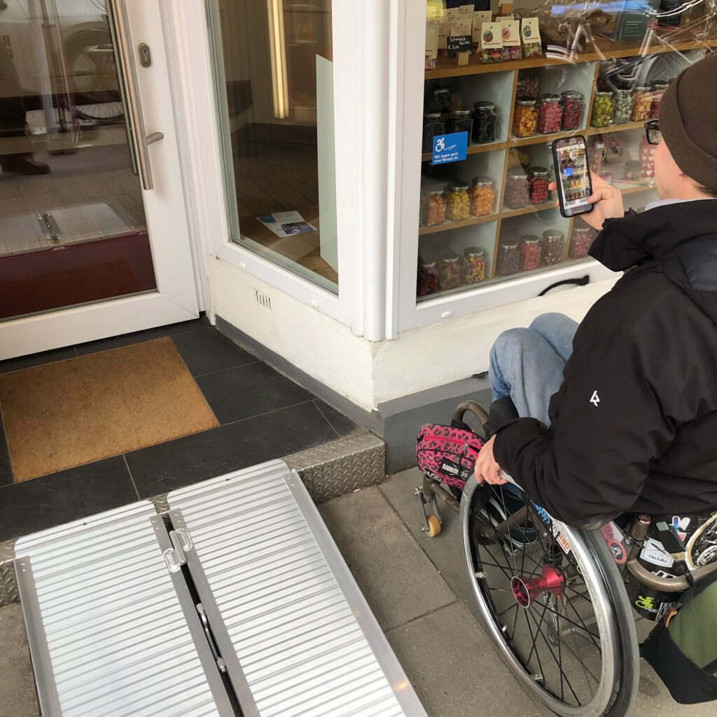 Ein Rollstuhlfahrer steht neben der Klapprampe, die den "Bonscheladen" barrierefrei erreichbar macht.