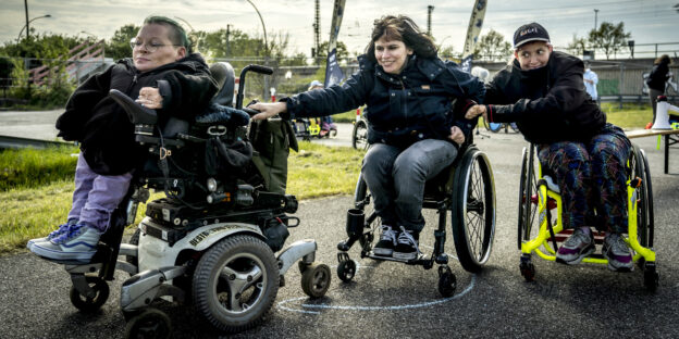 Eine Frau im Elektrorollsuhl zieht zwei Frauen in Rollstühlen ohne Motor